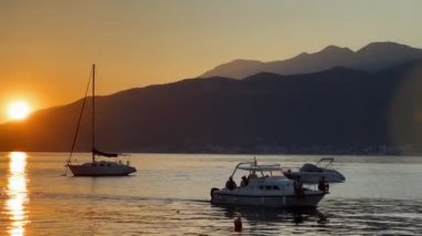 Boat with tourists sails past anchored yachts against the backdrop of mountains at sunset. High quality 4k footage