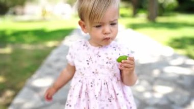 Little girl walks along a path in the park and eats a piece of lime. High quality 4k footage