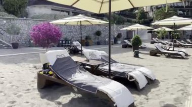Sun loungers covered with towels under a sun umbrella stand on the beach near the hotel. High quality 4k footage
