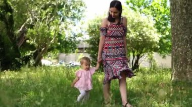 Mom teaches little girl to walk holding her hand in the garden. High quality FullHD footage