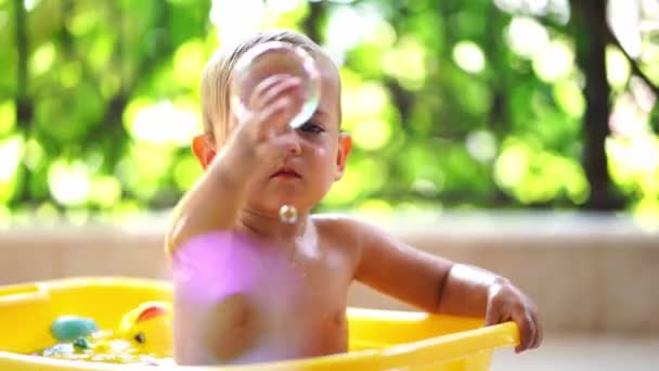 小女孩坐在一个盆子里 抓住肥皂泡 高质量的4K镜头 — 图库视频影像