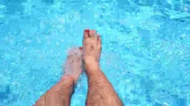 Men legs dangle on the turquoise water in the pool. High quality 4k footage