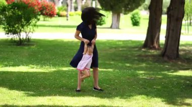 Annem yeşil bir çimenlikte ellerini tutarak küçük bir kızı sallıyor. Yüksek kalite 4k görüntü
