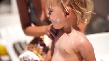 Mom smears sunscreen on the face and shoulders of a little girl. High quality 4k footage
