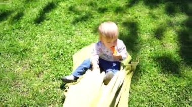 Little girl with a carrot in her hand is rolled on a blanket across the green grass. High quality 4k footage