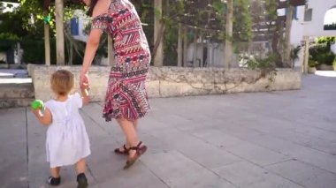 Mom takes the little girl by the hand and walks with her to the pergola in the garden. High quality FullHD footage