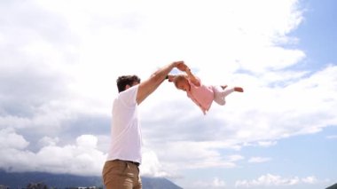 Dad shakes up and down a little girl by the arms high in the sky. High quality FullHD footage