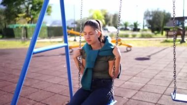 Young girl in thought swings on a chain swing in the park. High quality 4k footage