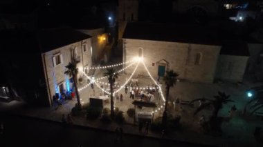 Guests dance in the courtyard at a wedding celebration under the lighting of garlands of light bulbs. High quality 4k footage