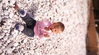 Little girl sits on a pebble beach and knocks a stone against a stone. High quality 4k footage