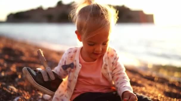 小女孩坐在海滨时把运动鞋穿在腿上 高质量的4K镜头 — 图库视频影像