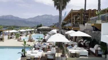 Double sun loungers stand near the pools under sun umbrellas against the backdrop of the mountains. High quality 4k footage