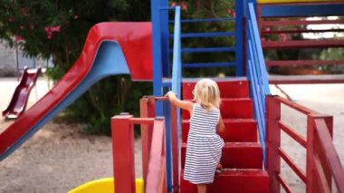 Little girl walks up the stairs to the slide, holding on to the railing. Back view. High quality 4k footage