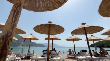 People sit on the beach by the sea under straw sun umbrellas. High quality 4k footage