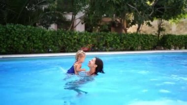 Mom lifts a little girl in her arms while standing in the pool. High quality 4k footage