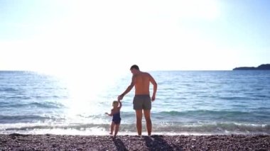 Dad with a little girl holding hands go into the surf. High quality 4k footage