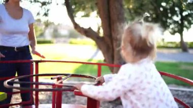 Mom spins a carousel with a little girl sitting on it on the playground. High quality 4k footage