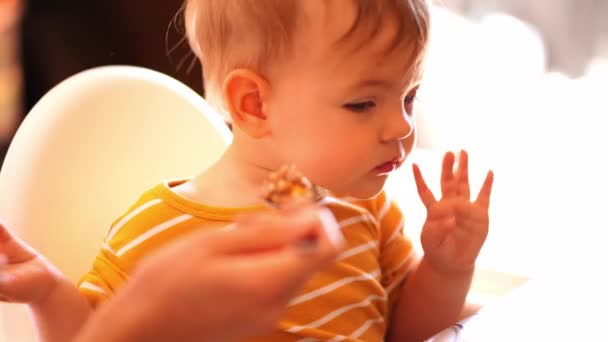 高い椅子の上の赤ん坊は母親からお粥とスプーンを取って食べます 高品質4K映像 — ストック動画