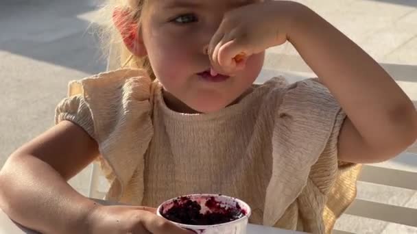 テーブルの椅子に座りながらカップからアイスクリームを食べる少女 高品質4K映像 — ストック動画