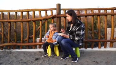 Mom feeds a little girl from a spoon while sitting on chairs near the fence. High quality 4k footage