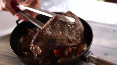 Woman removes roast beef from the pan with tongs and puts it on a plate. High quality 4k footage