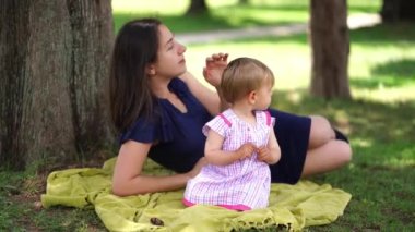 Mom lies on a blanket under a tree next to a little girl sitting. High quality 4k footage