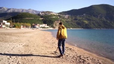 Man with a metal detector walks along the beach against the backdrop of mountains. High quality 4k footage