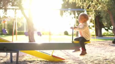 Little girl swings on a swing-balancer, holding the handle. High quality 4k footage
