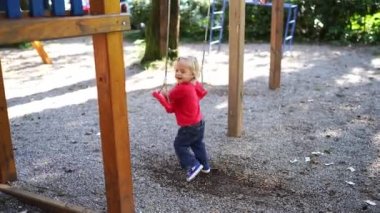 Little girl swings on her stomach on a swing, kicking off with her feet in the playground. High quality 4k footage