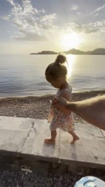 Little girl walks barefoot along a stone curb above the beach, holding her father hand. High quality 4k footage
