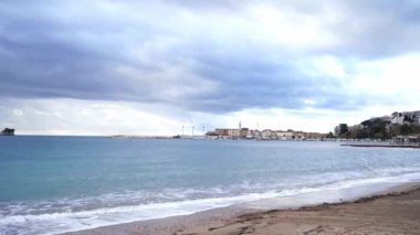 Bulutlu bir gökyüzüne karşı sahilden Budva 'nın eski şehrine bakın. Karadağ. Yüksek kalite 4k görüntü