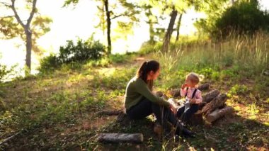 Mother and little daughter are sitting on stumps in a sunny meadow. High quality 4k footage