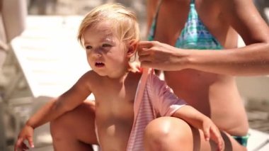 Mom puts summer overalls on a little girl sitting on a sun lounger. High quality 4k footage