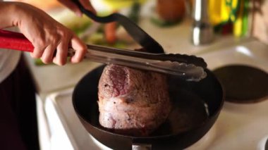 Kadın, yanında spatula ve kızartma tavasında maşayla pişen bir bifteğe basıyor. Yüksek kalite 4k görüntü