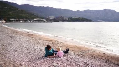 Anne ve küçük kız çakıl taşı plajında oturmuş çakıl taşlarını ayırıyorlar. Yüksek kalite 4k görüntü