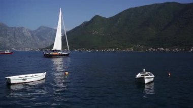 Small sailing yacht sways on the sea waves against the backdrop of mountains. High quality FullHD footage