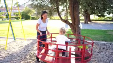 Smiling mother rides a little girl on a carousel in the playground. High quality 4k footage