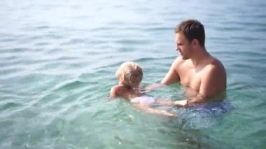Dad teaches a little girl to swim in the sea, holding her in his arms. High quality 4k footage