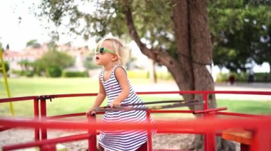 Little girl in sunglasses rides a carousel in the park, turning the steering wheel. High quality 4k footage