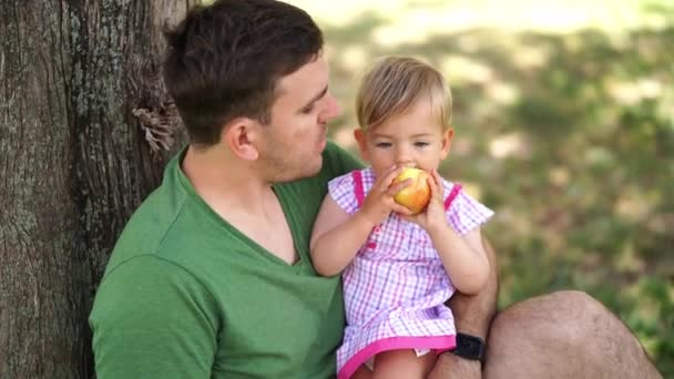 Κοριτσάκι Αντιμετωπίζει Τον Μπαμπά Ένα Μήλο Ενώ Κάθεται Στην Αγκαλιά — Αρχείο Βίντεο