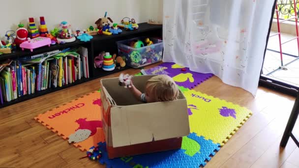 Klein Meisje Zit Een Grote Doos Kamer Gooit Speelgoed Uit — Stockvideo