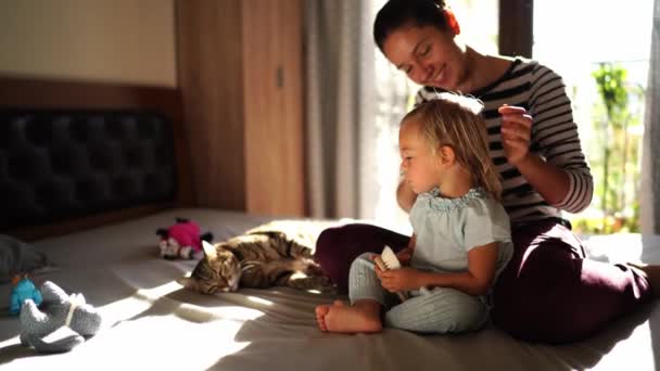 Маленькая Девочка Пытается Причесать Свою Кошку Сидя Кровати Пока Мама — стоковое видео