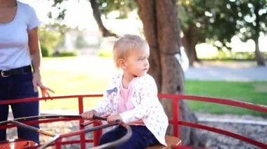 Mom rides a little girl sitting on the seat and holding the steering wheel on a carousel. High quality 4k footage