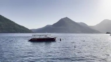 Small excursion boat is moored near the shore against the backdrop of mountains. High quality 4k footage