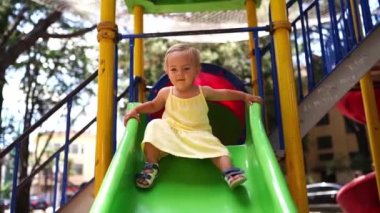 Little girl in a yellow dress slides down a slide. High quality FullHD footage