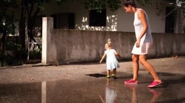 Little girl with her mother walk through the puddles in the courtyard of the house and splash. High quality 4k footage
