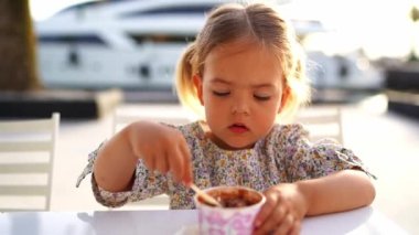 Little girl eats ice cream with a spoon from a cup. High quality FullHD footage