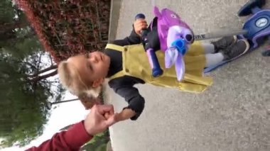 Dad carries a little girl on a scooter along an asphalt road in the park. High quality 4k footage