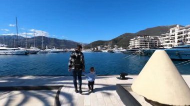 Mom and a little girl stand on the pier and look at the sea and moored yachts. High quality 4k footage