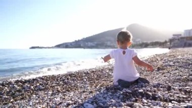 Little girl sits on her knees on a pebbly beach and picks at the stones with a stick. High quality 4k footage